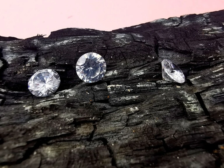 Three cut diamonds resting on dark charcoal, illustrating lab-grown versus natural diamond origins